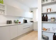 A long shot of a stylish kitchen with white work tops and ample storage.