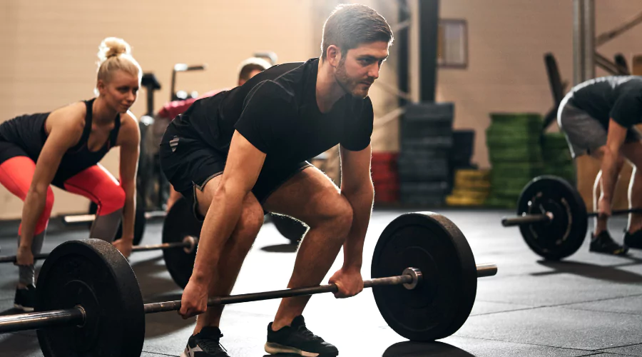 Small strength class with focus on male in black active wear preparing to do a deadlift..