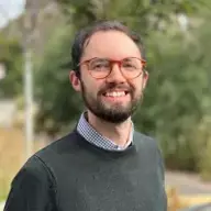 Close up photograph of a smiling young man with brunette hair and glasses