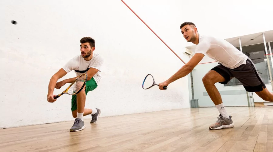 Two men playing squash on the court in a lunge position ready to hit the squash ball.