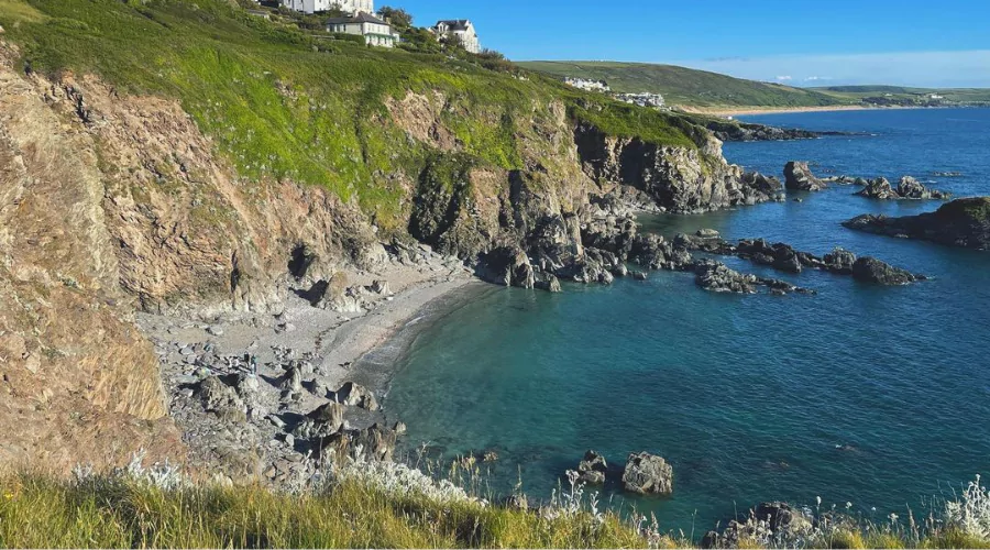 View down onto a rugged pebble beach with a bay of dark-blue sea water