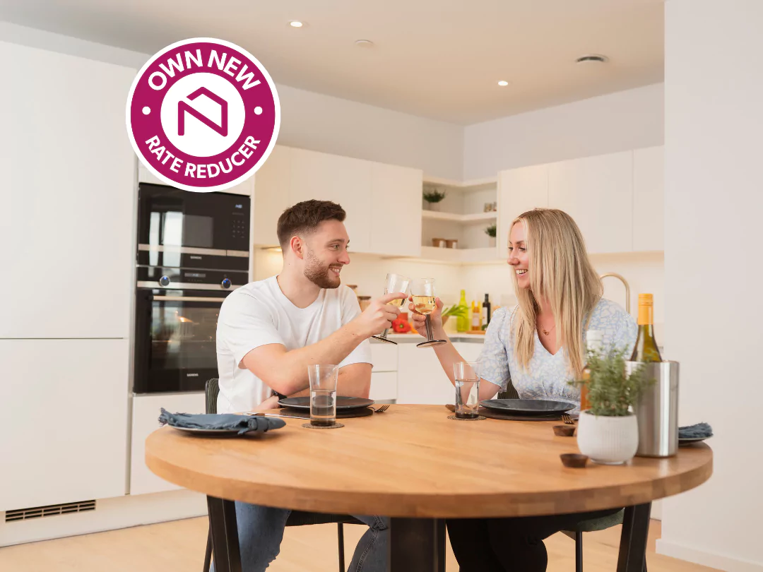 Young mixed-sex couple raising a toast while sat at the dining table in a contemporary white kitchen-diner