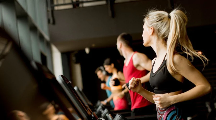 Woman with blonde hair running on treadmill in the gym looking toward other gym members also running on other treadmills.