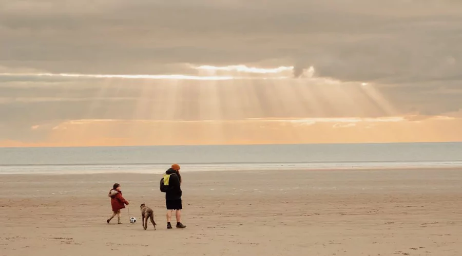 Man, child and dog on a flat sandy beach wrapped in warm winter clothing