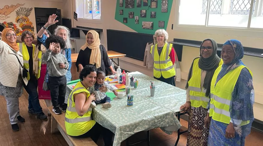 Group of refugee women, charity workers and children smiling and waving at the camera.