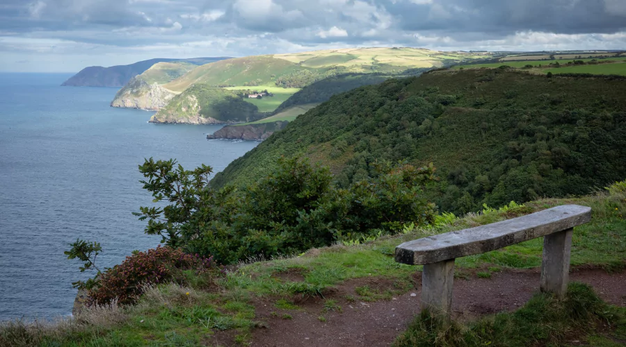 Empty wooden bench on the headland looking out to sea and the sunny coastline in the distance