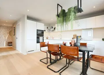 Open-plan kitchen diner with glossy white work tops, hanging plants and stylish seating.