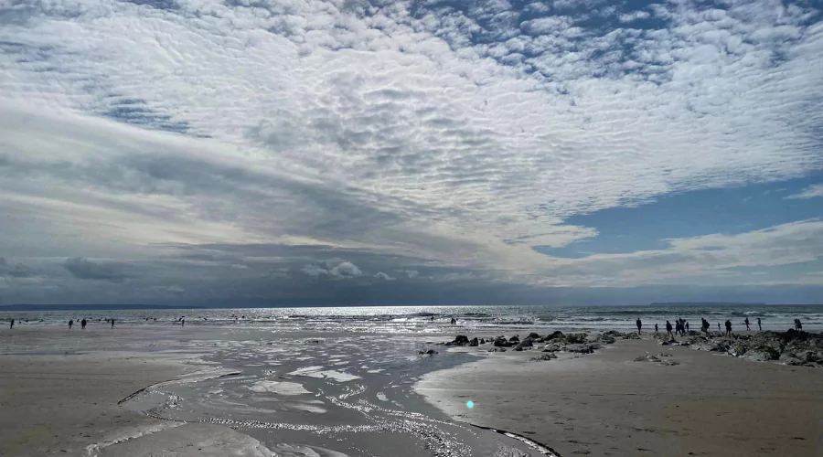 View out across a flat, golden sandy beach with stream running down into the sea