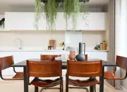 Close up of a styled dining table complemented by hanging plants and an open-plan kitchen.