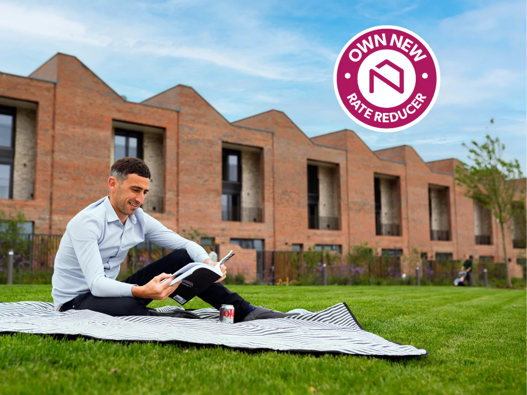 Man sat on a picnic blanket reading a book in a green space at Brabazon Bristol